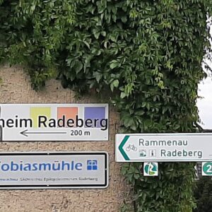 Wegweiser an einer Hauswand mit Hinweisschild zum Tierheim Radeberg (200 m nach links) sowie weiteren Richtungsschildern nach Rammenau und Radeberg.